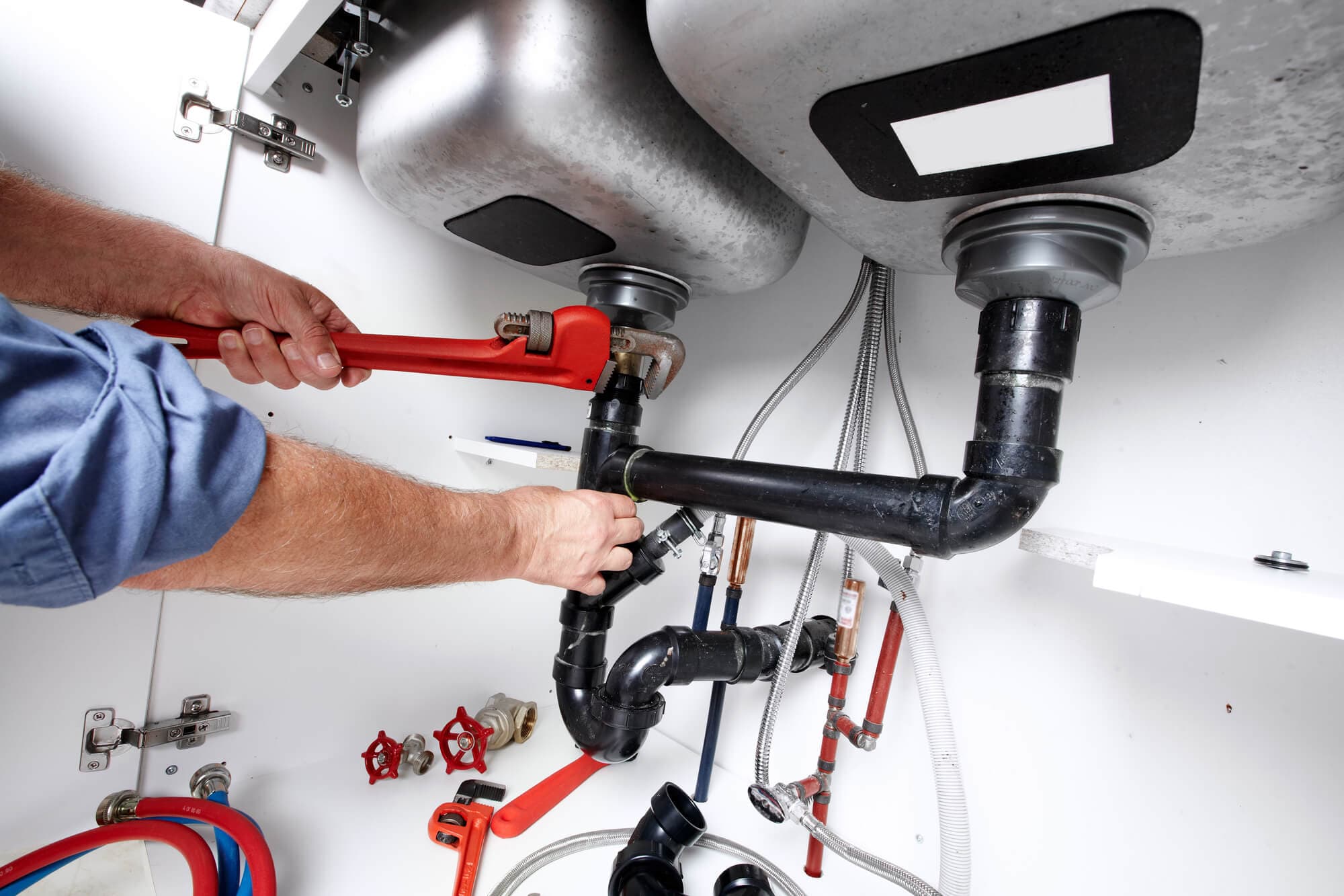 Licensed plumber repairing under-sink pipes with a professional pipe wrench