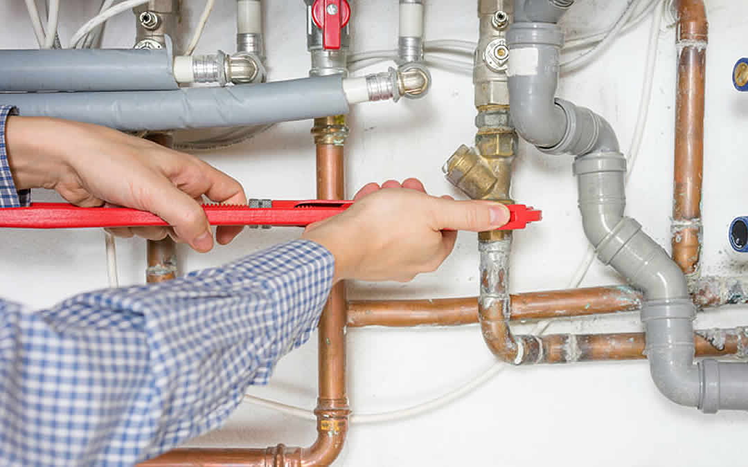 Plumber tightening copper and PVC pipes on a boiler system